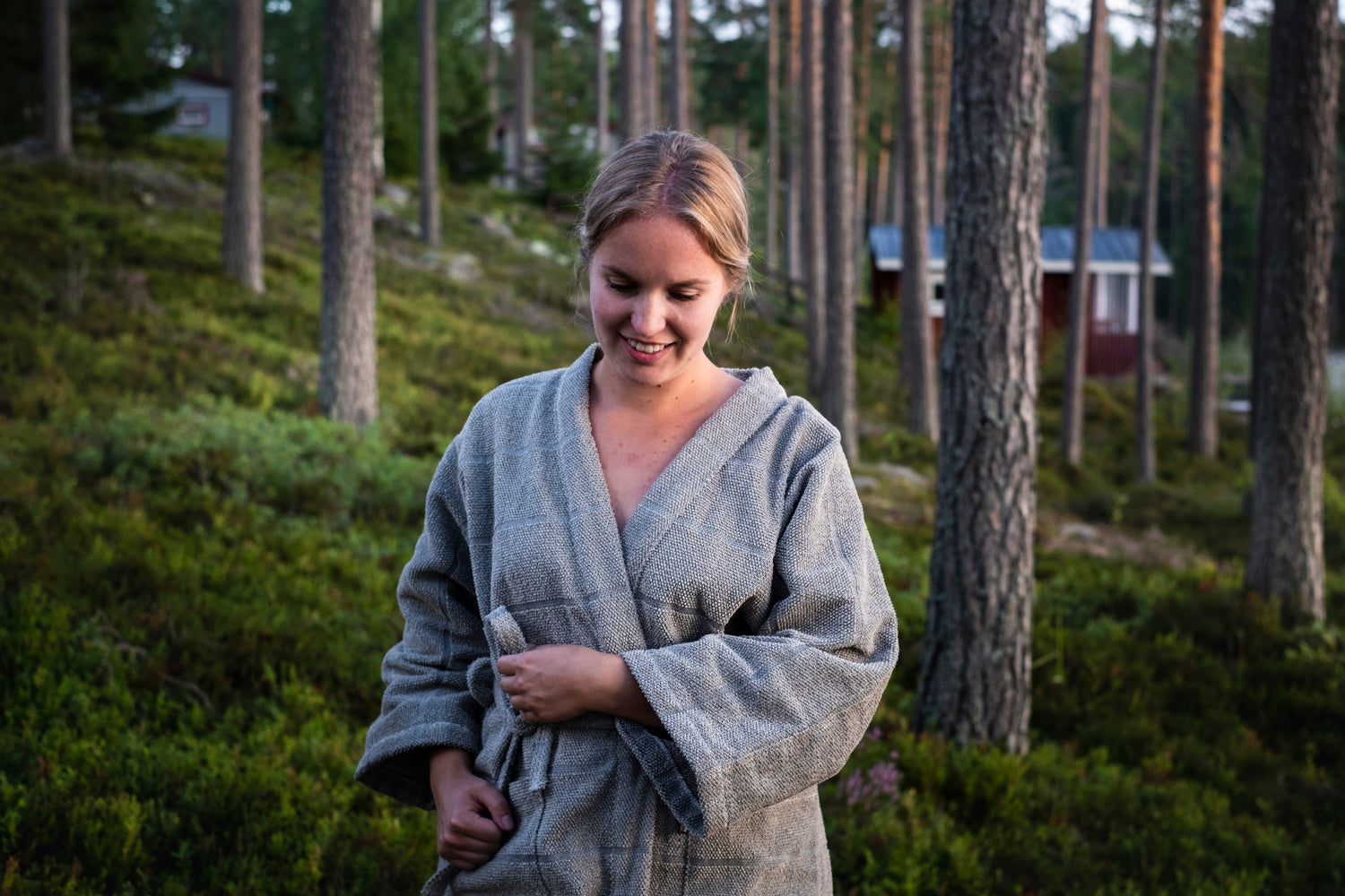 Nainen pellavakylpytakki päällä kävelee suomalaisessa mäntymetsässä